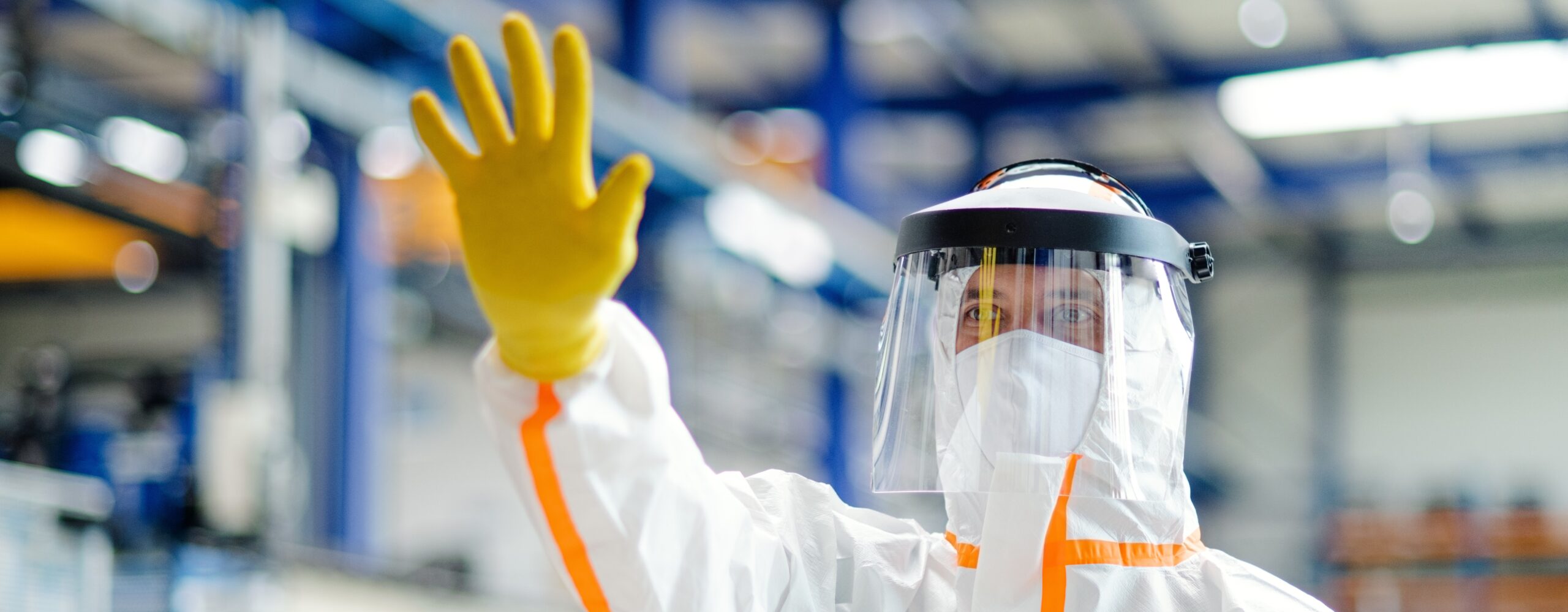Front view of worker with protective mask and suit in industrial factory, greeting hand gesture.